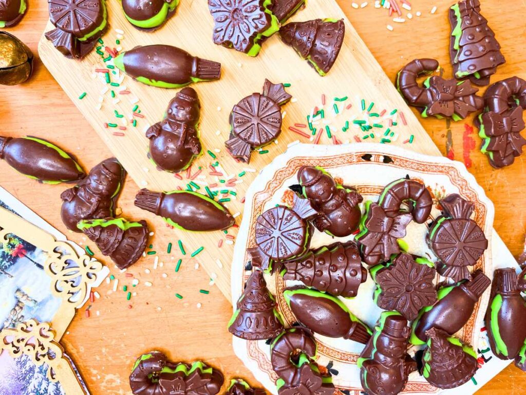 An arrangement of molded mint chocolate candies. Some are on a wooden cutting board and some are on a brown floral plate.