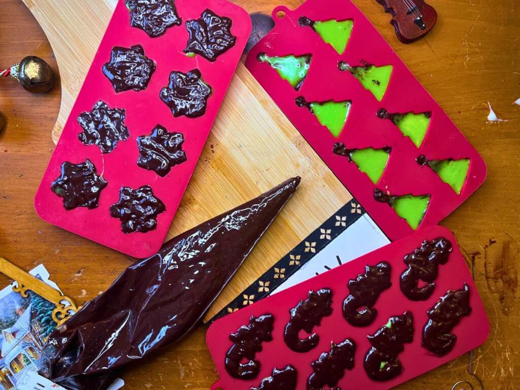 Mint chocolate candies in some red silicone candy molds. There is a piping bag full of melted chocolate.