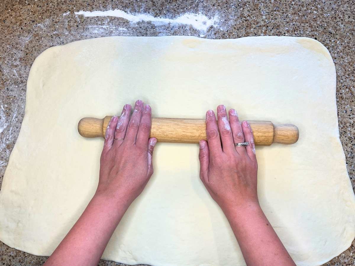 A woman is rolling out dough into a rectangle.