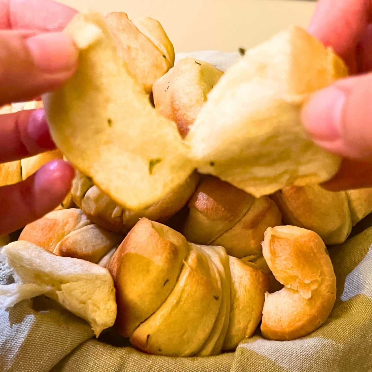 A woman is pulling apart a dinner roll.