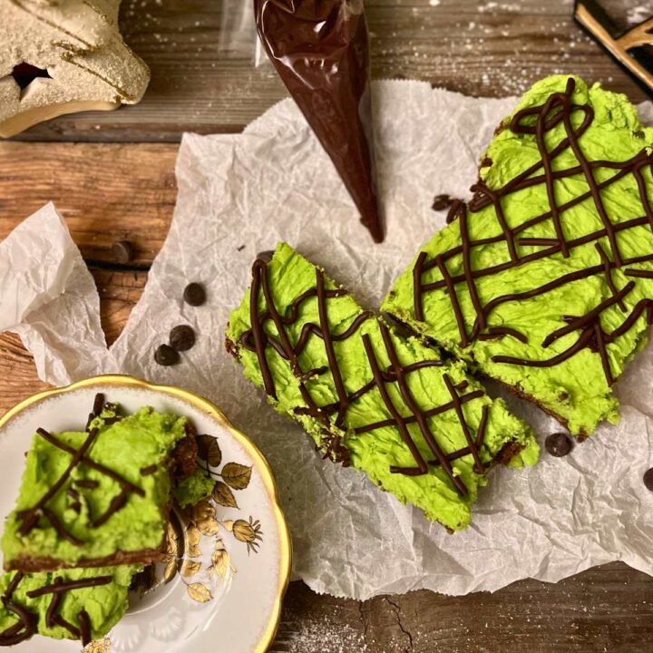 Green mint chocolate squares sliced on a piece of parchment paper. There is a piping bag with chocolate inside.