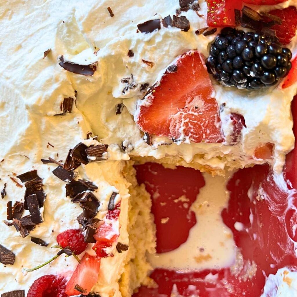 A tres leches cake with berries on top. There is a slice removed.