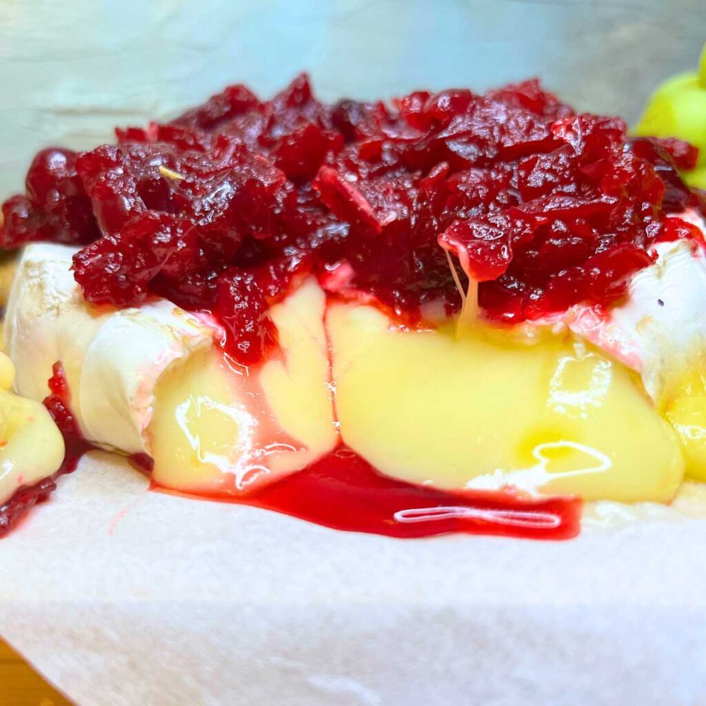 A baked Brie wheel of cheese covered in cranberry sauce. There is a slice out of the front.