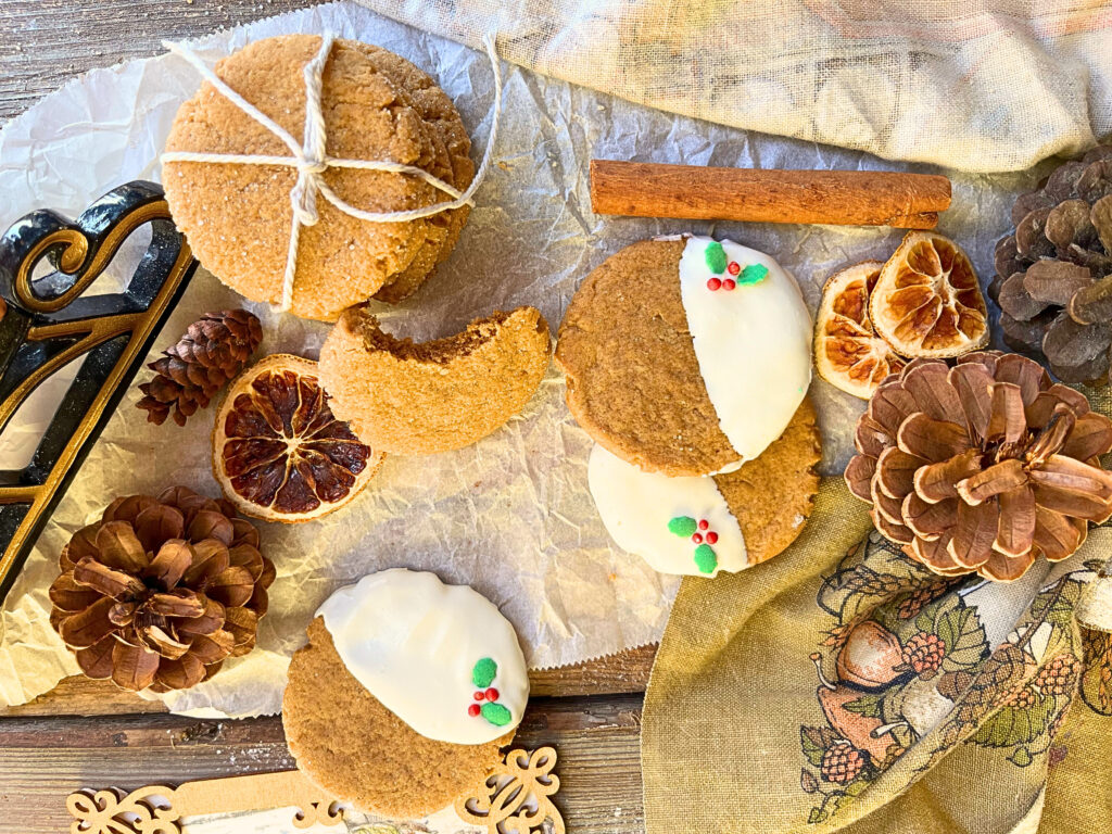 A table display of gingerbread cookies. Some decorated with white chocolate and Christmas sprinkles. Some are plain and wrapped in kitchen twine. One has a bite out of it.