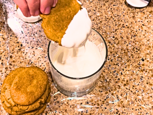 Woman dipping a gingerbread cookie into a glass with melted white chocolate.