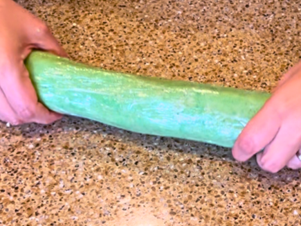 Woman forming mint shortbread cookie dough into a log shape wrapped in cling-film.