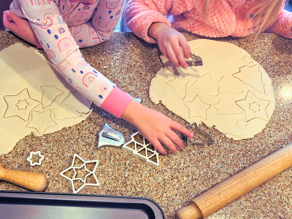 Two children cutting out salt dough shapes using cookie cutters.