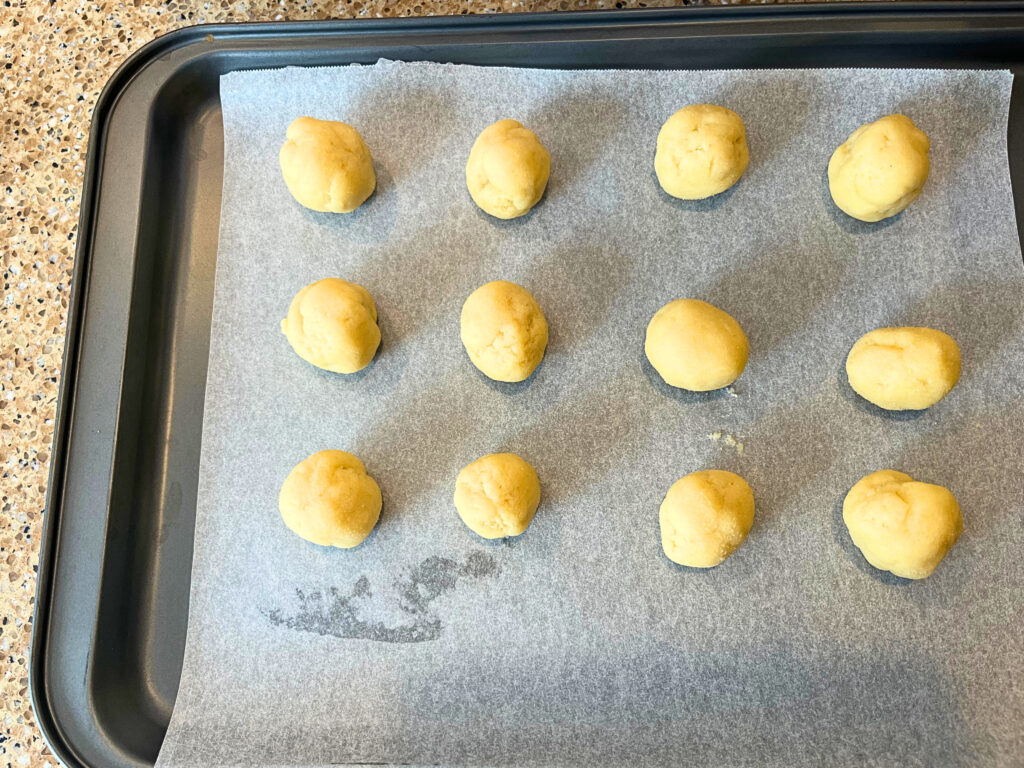 Rolled dough balls on a lined baking sheet.