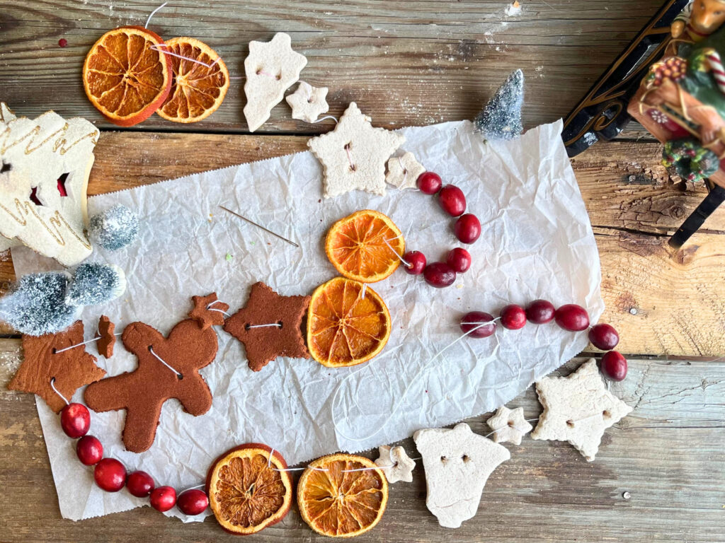 Natural DIY garland on a wooden table. The garland features dried orange slices, cinnamon figures, salt dough decorations, and cranberries.