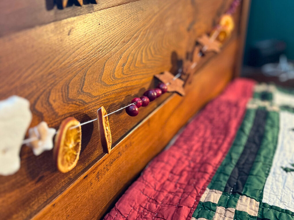 Homemade garland, featuring salt dough, cinnamon dough, cranberries, and dried orange slices, displayed at the headboard of a bed.