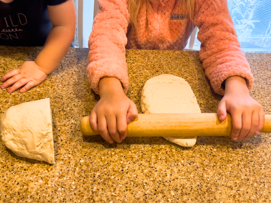 A child rolling out salt dough with a wooden rolling pin.