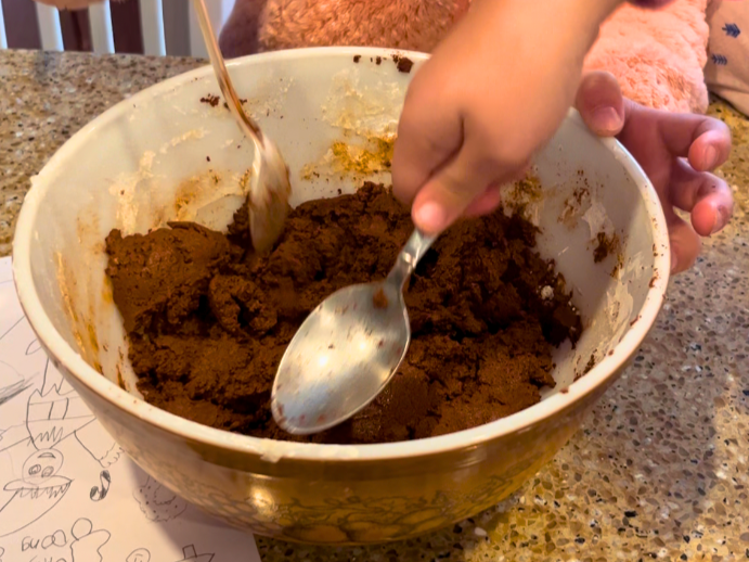 Children mixing cinnamon dough in a large brown bowl.