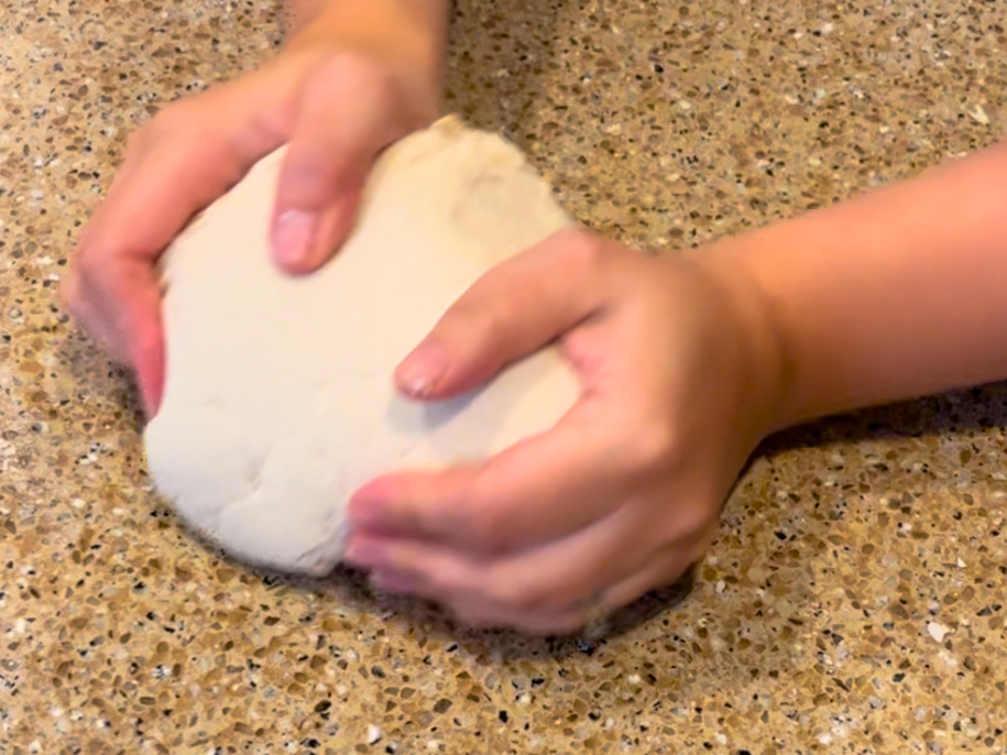 Woman kneading salt dough on a brown counter top.