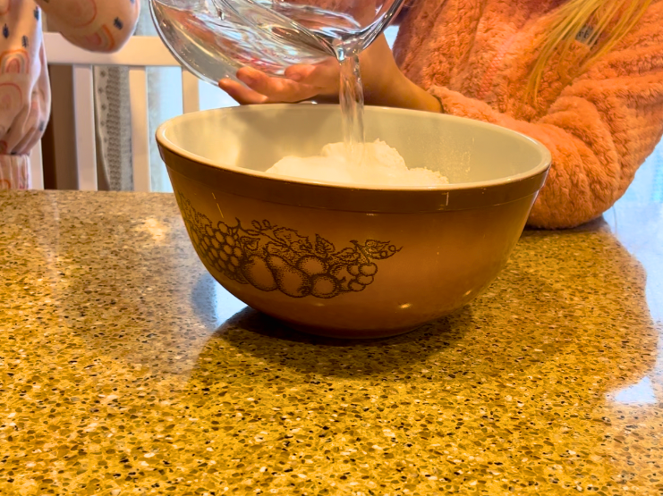 A child pouring warm water into a bowl with flour and salt.