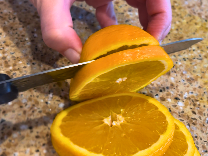 Woman slicing an orange with a kitchen knife.
