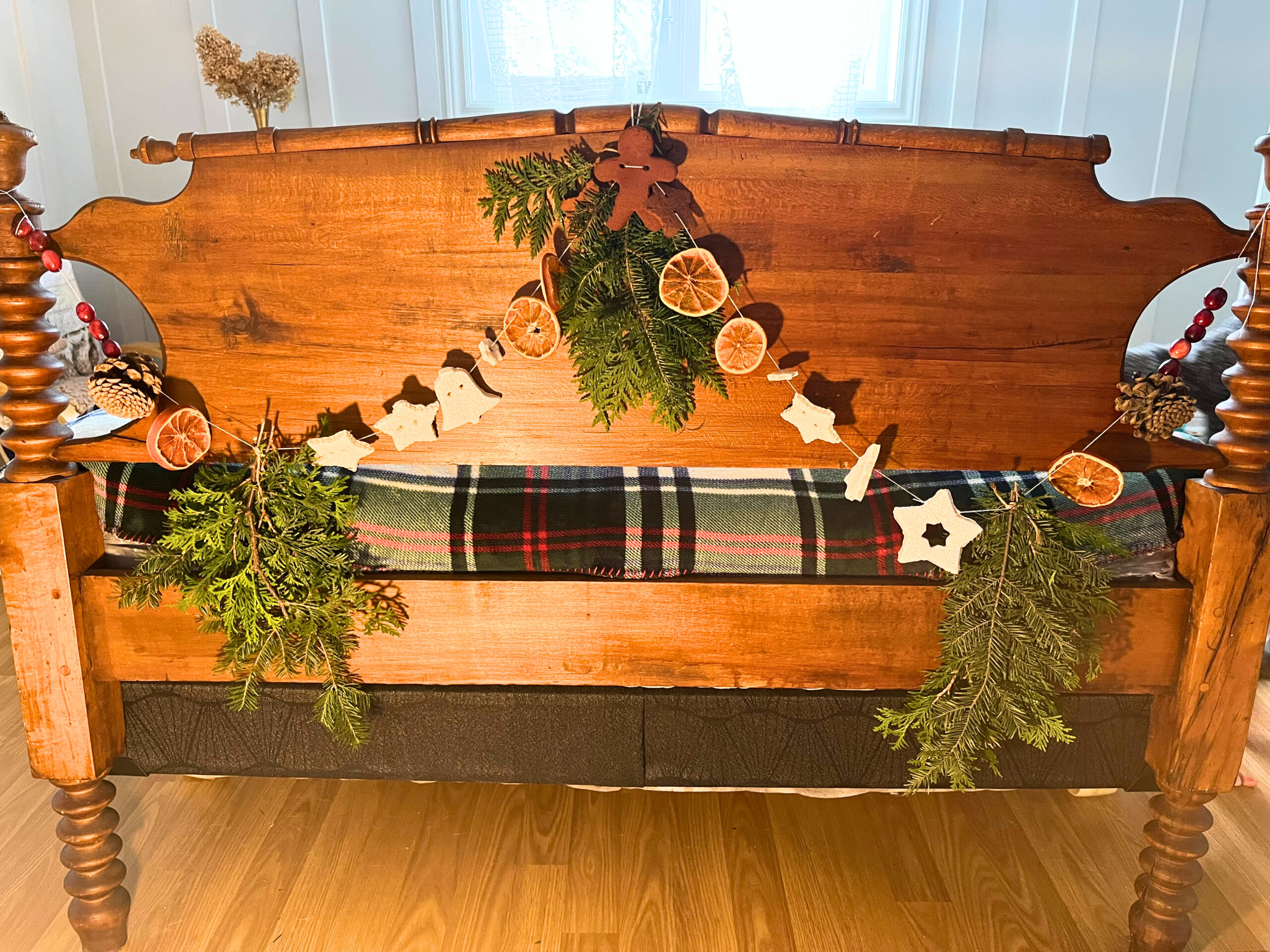 Natural Christmas garland tied to a bed footboard. It consists of orange slices, cranberries, salt dough, cinnamon dough, and pieces of evergreen.