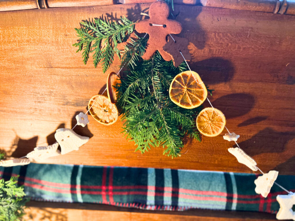 Natural Christmas garland tied to a bed foot board. There is evergreen, salt dough, cinnamon dough, dried orange slices, and cranberries attached together with a piece of embroidery floss.