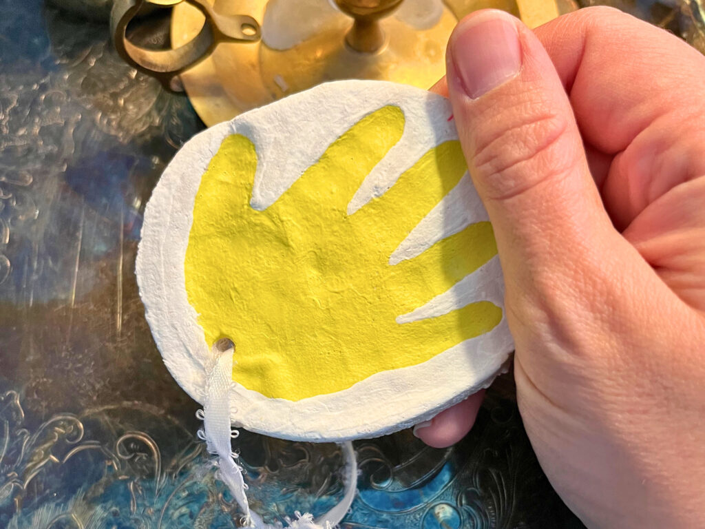 Woman holding a salt dough ornament with a yellow handprint on it.