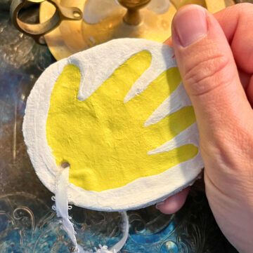 Woman holding a salt dough ornament with a yellow handprint on it.