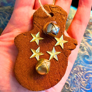 Woman holding a cinnamon dough ornament in the shape of a snowman. It is decorated with stars and bells.
