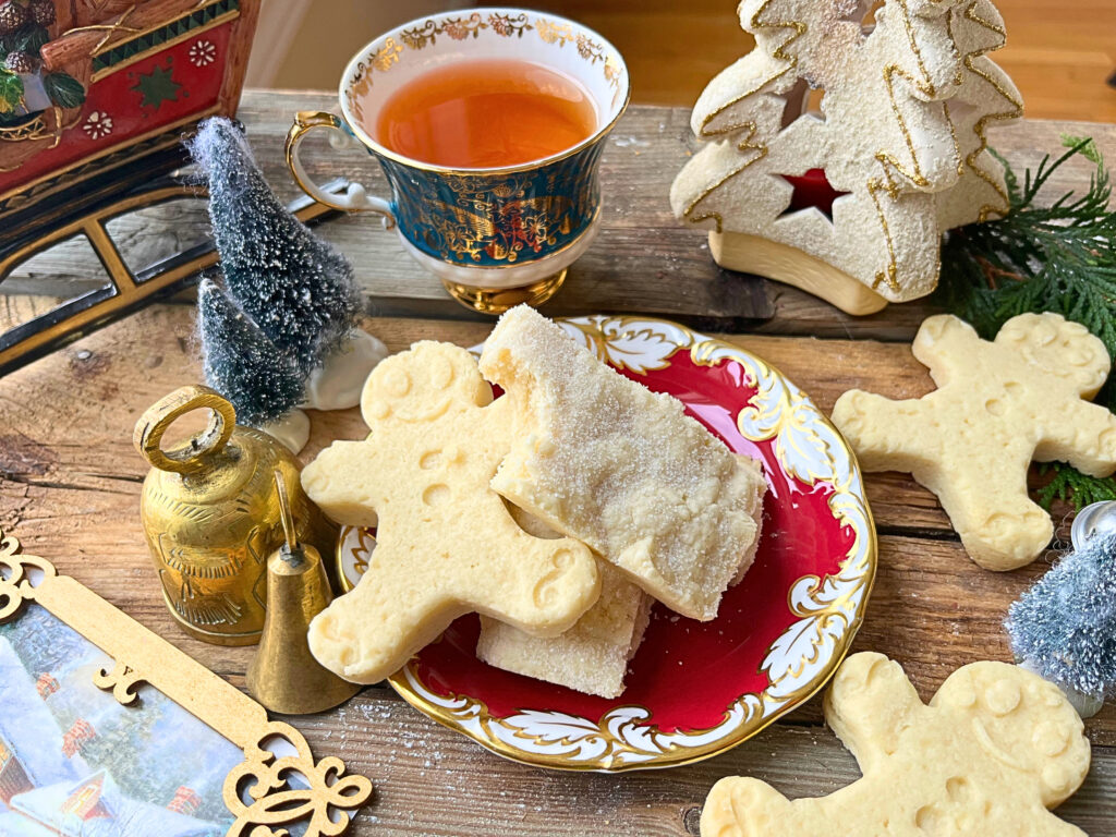 A red plate with shortbread cookies some rectangular and some in the shape of gingerbread men. A cup of tea in the background. 