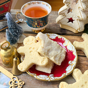 A red plate with rectangular shortbread cookies and some gingerbread man shaped shortbread cookies. A cup of tea in the background.