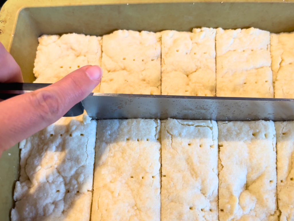 Woman marking cuts into baked sugar cookies, with a kitchen knife.