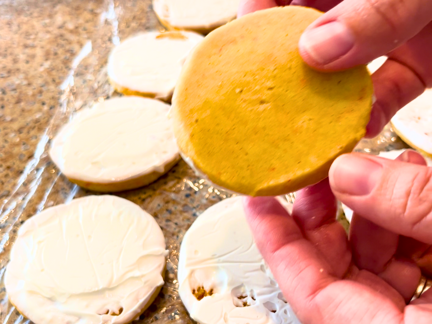 Woman holding an orange and cardamom shortbread cookie. More cookies i the background.