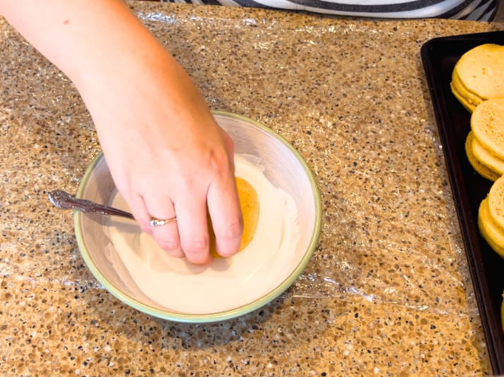 Woman dipping orange cardamom cookies in a bowl of melted white chocolate.