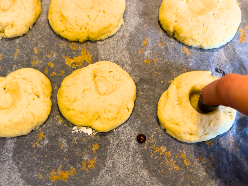 Woman pressing a thimble into the centre of baked thumbprint cookies.