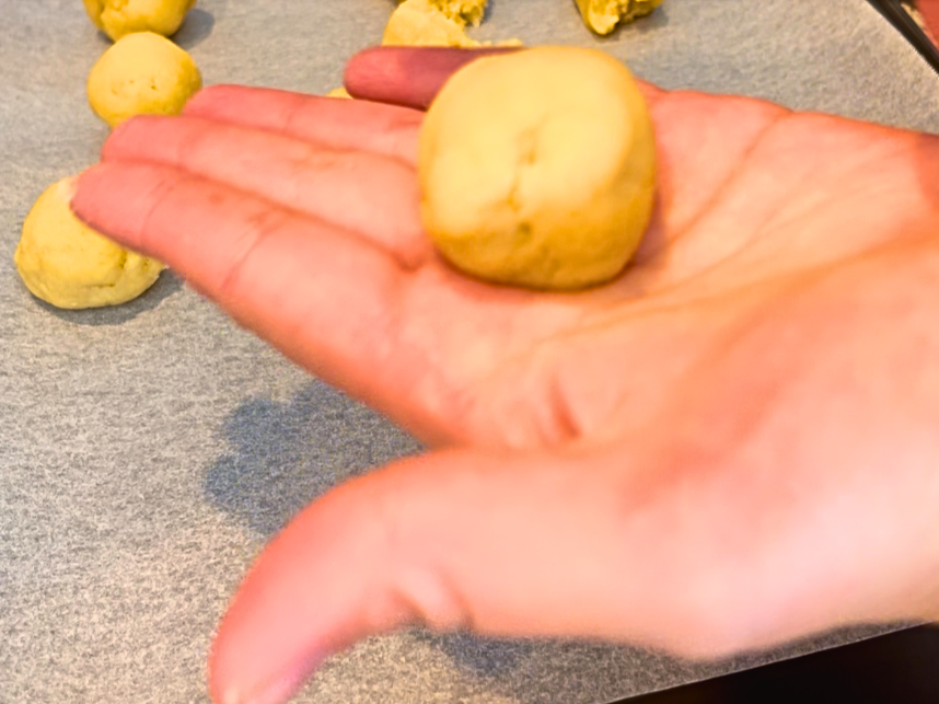Woman holding a dough ball. More dough balls on a parchment lined baking sheet in the background.