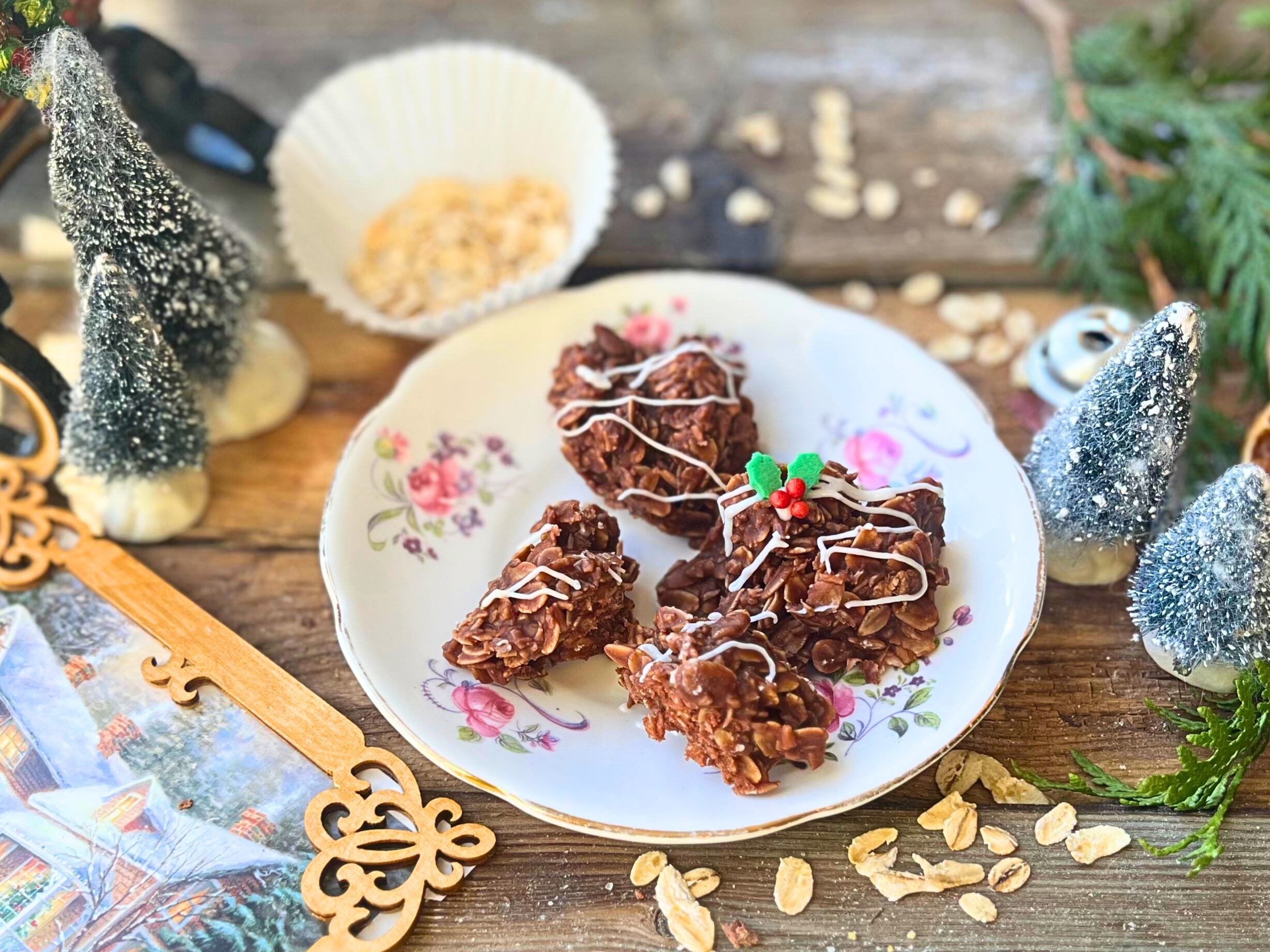 A white and pink floral plate with four chocolate haystacks on it. They are all decrated with a white icing drizzle and one has a festive holly decoration.