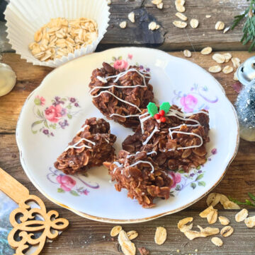 A white and pink floral plate with four chocolate haystacks on it. They all have a white icing drizzle and one is decorated with holly sprinkles.