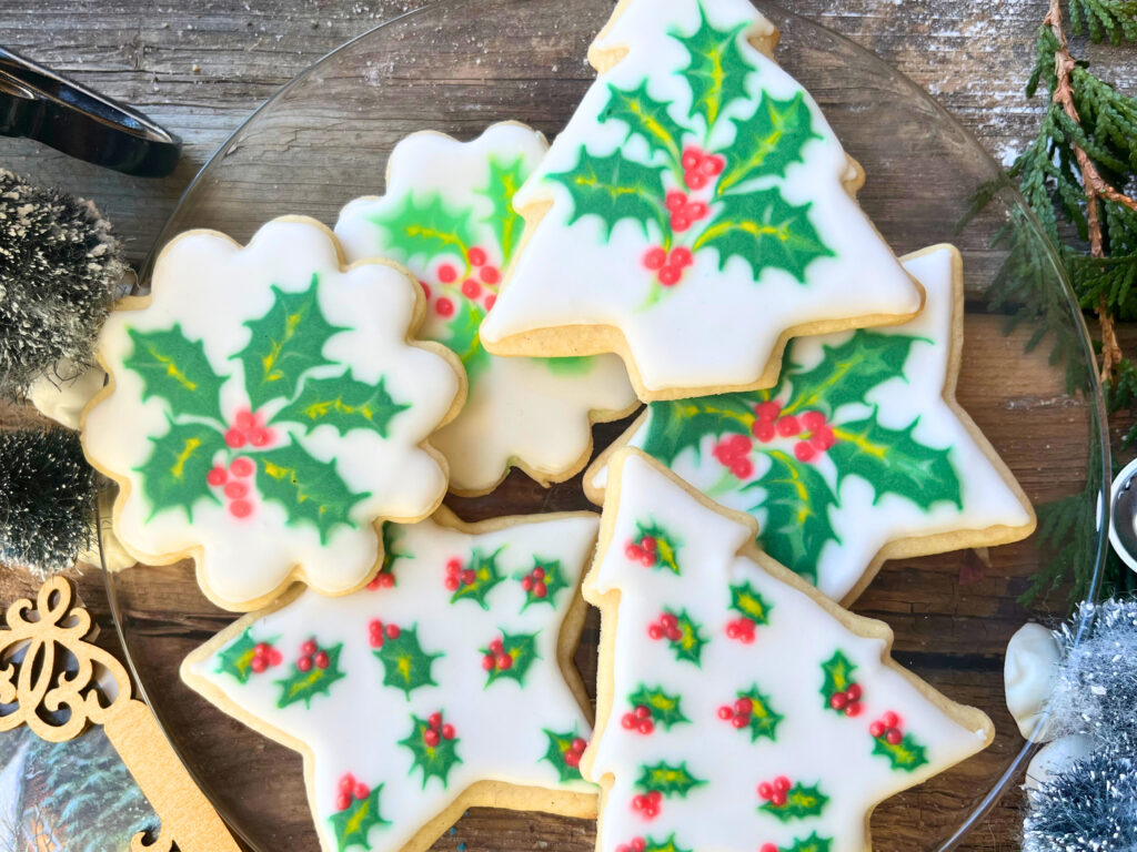 A glass plate with holly decorated sugar cookies with royal icing.