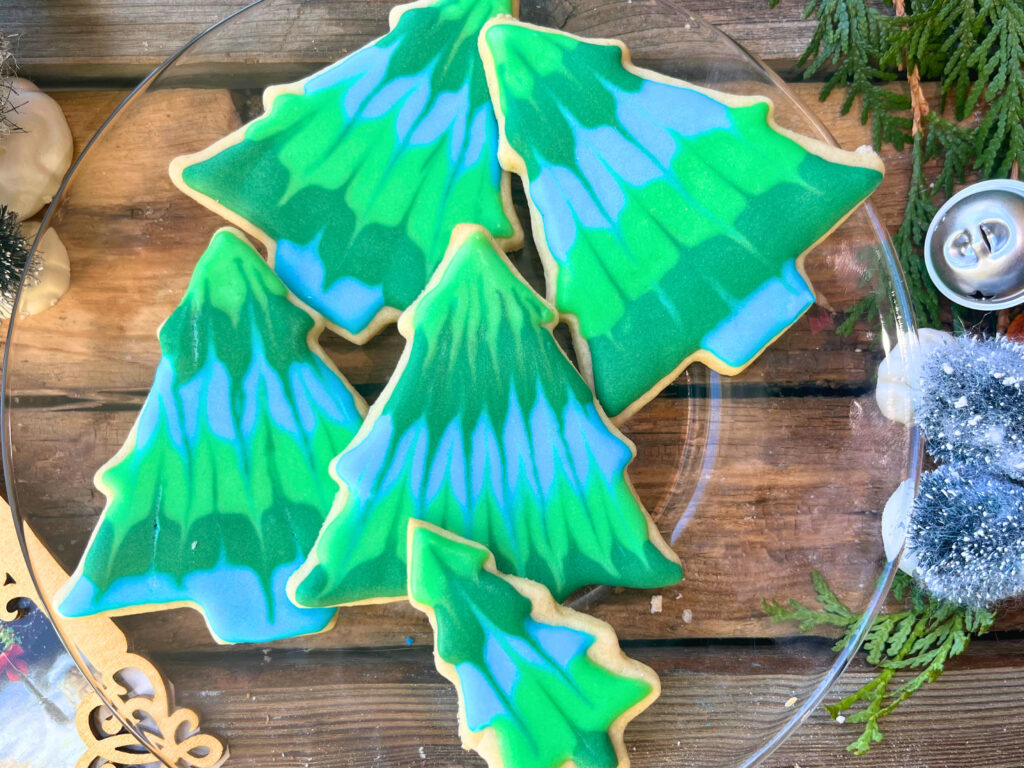 A glass plate with decorated Christmas tree sugar cookies with royal icing.
