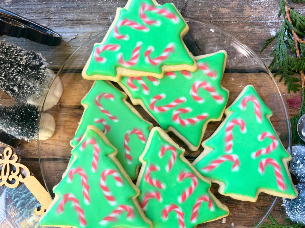 A glass plate with Christmas tree candy cane decorated sugar cookies with royal icing.
