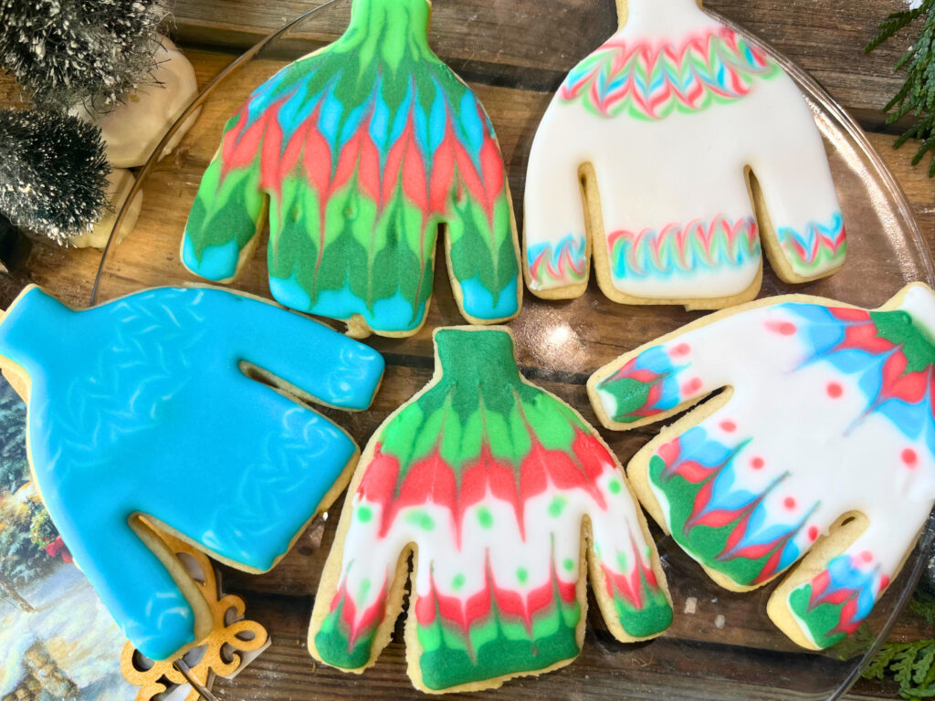 A glass plate with decorated winter sweater sugar cookies with royal icing.