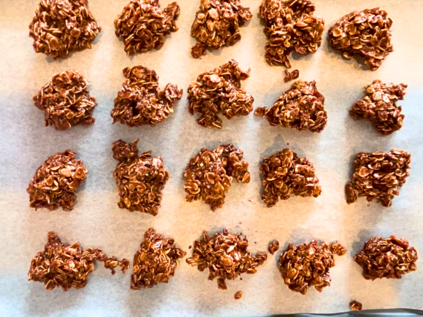 A baking sheet with parchment paper filled with chocolate haystacks.