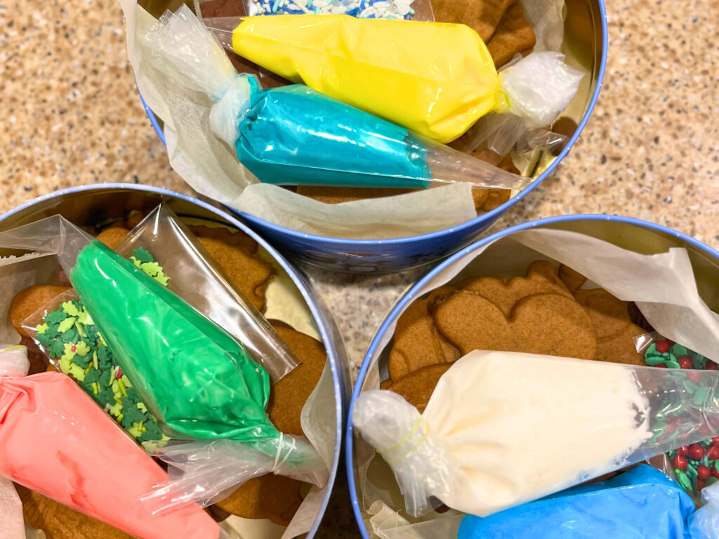 Three cookie tins with gingerbread cookies and coloured icing in piping bags.