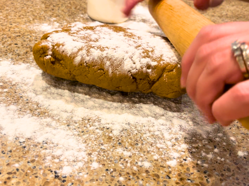 Woman rolling out gingerbread cookie dough with a wooden rolling pin.