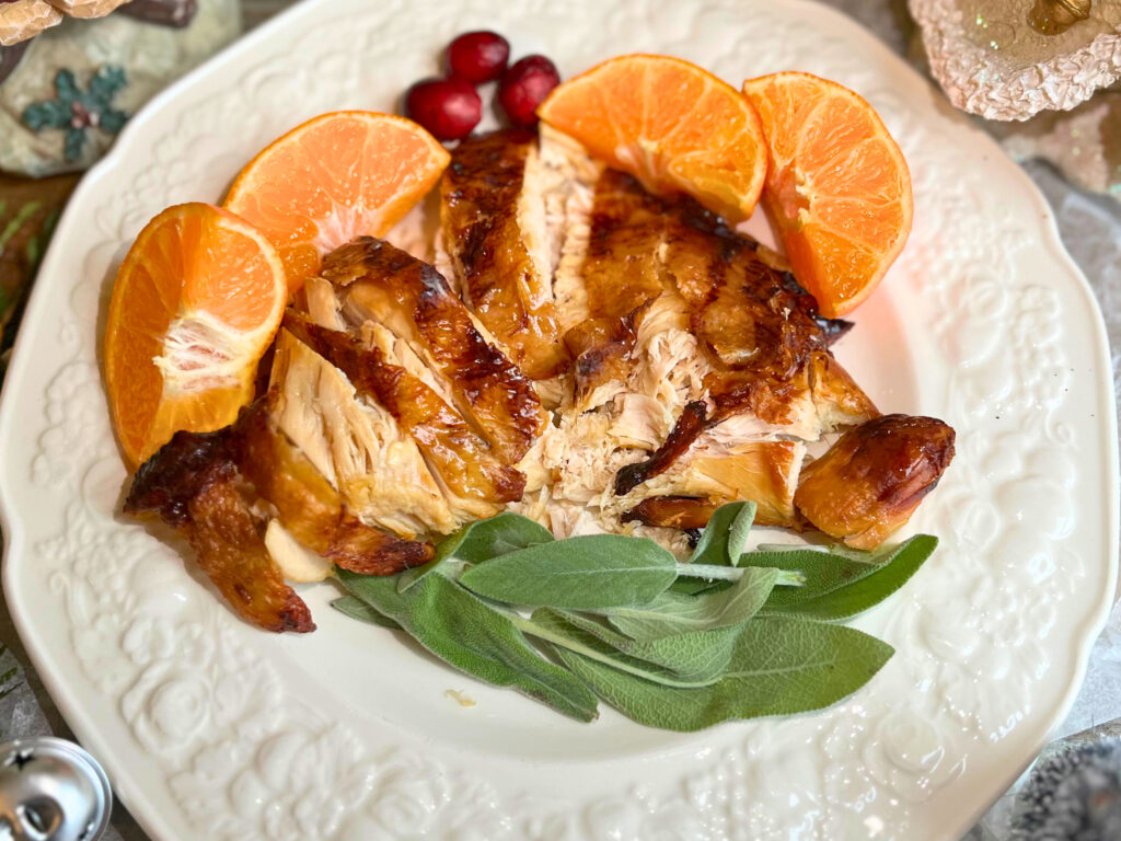 A plate with sliced turkey breast. Some sage leaves in the foreground and clementines and cranberries in the background.