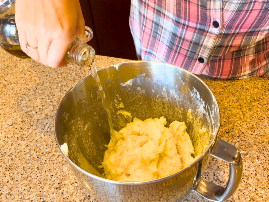 Woman pouring vanilla extract into a bowl of creamed butter, sugar, and eggs.