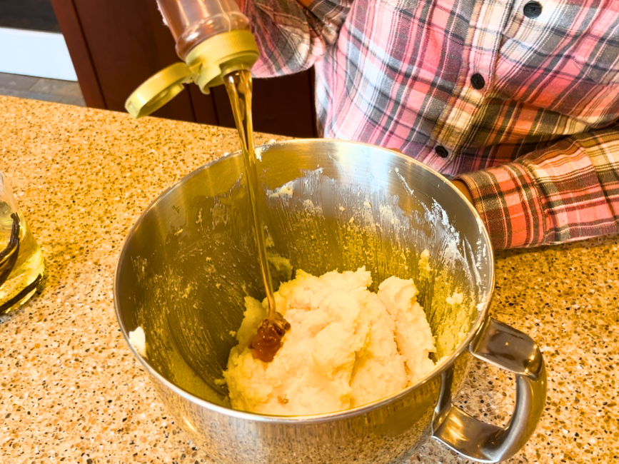 Woman adding corn syrup in to a bowl of creamed butter, sugar, and eggs.