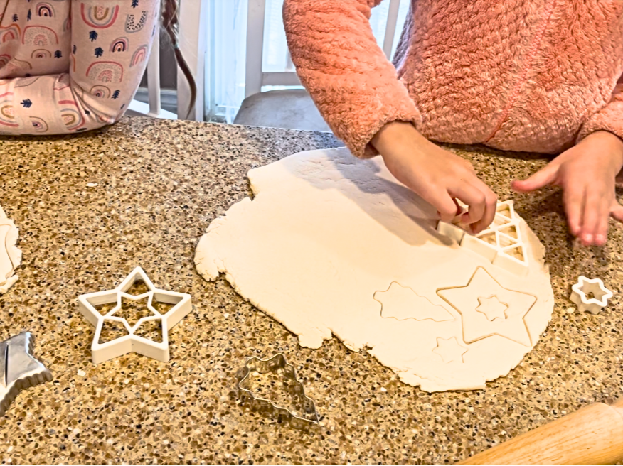 A child cutting out cookies using cookie cutters.