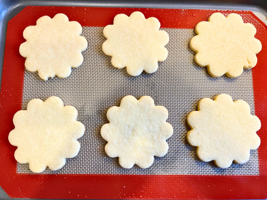 Six sugar cookies on a baking sheet with a non-stick mat.