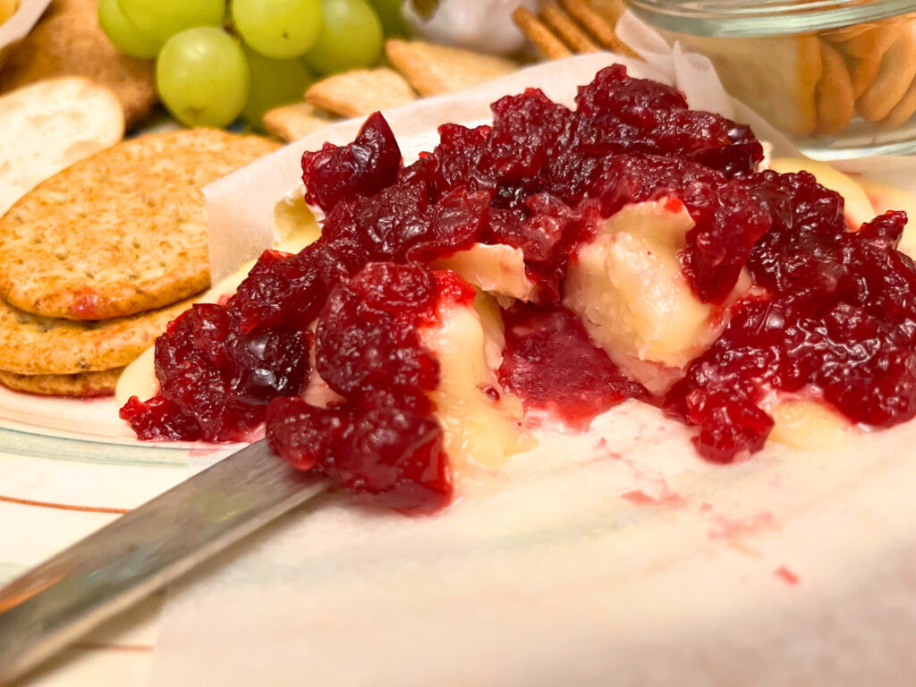 Baked brie with cranberry sauce. Crackers and grapes in the background.