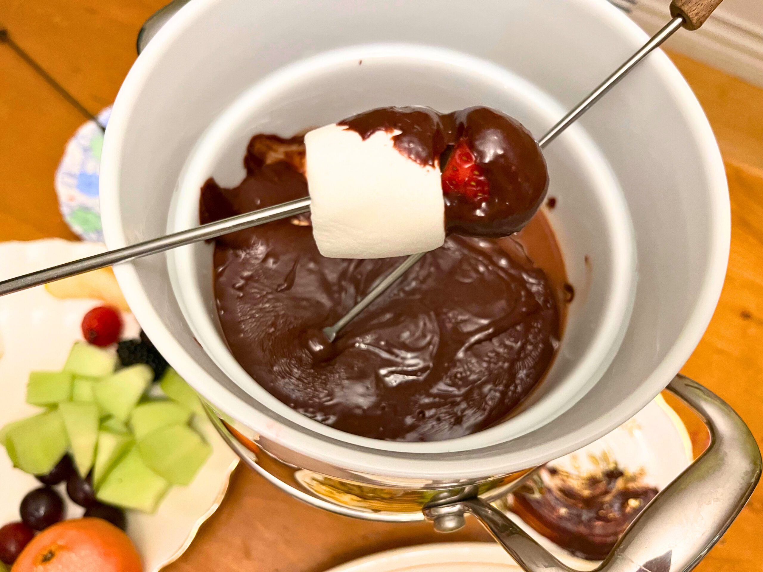 Someone dipping marshmallow and strawberry into a chocolate fondue.