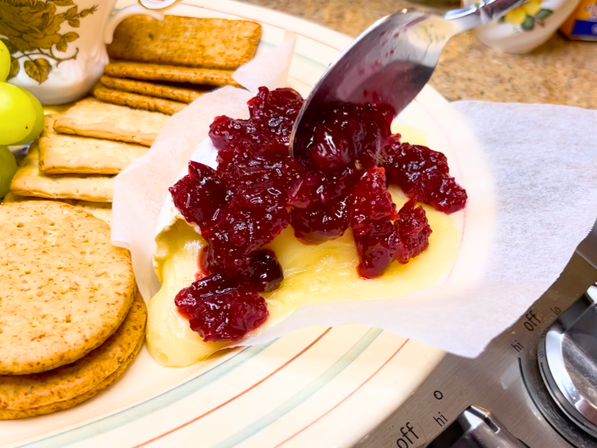 Woman spooning cranberry sauce onto a wedge of baked brie.