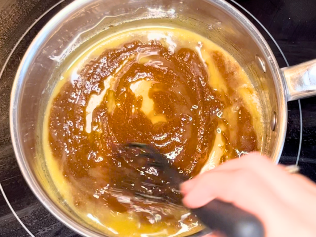 A woman stirring melted butter and brown sugar in a sauce pot.