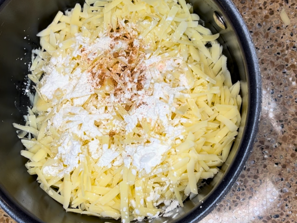 Shredded Swiss cheese in a sauce pot with cornstarch, nutmeg, and salt and pepper.